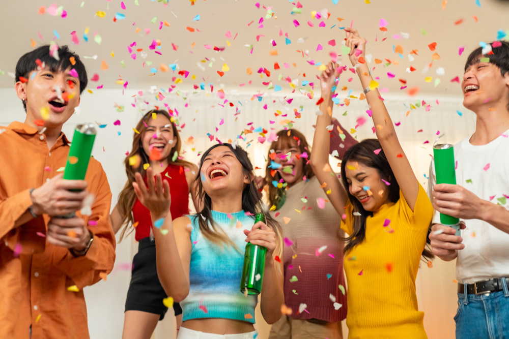 Group of Happy young Asian man and woman friends college student enjoy and fun celebration holiday event meeting party dancing and playing confetti together in living room at home on vacation night