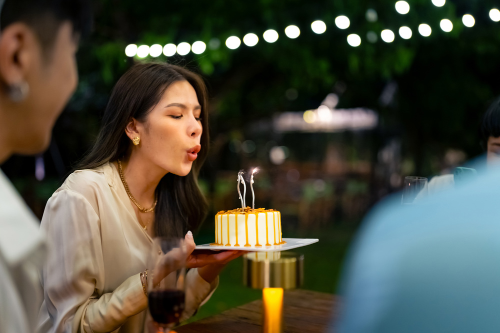 Group of Happy Asian millennial people friends enjoy and fun celebration birthday party at dinner party the garden at restaurant. Beautiful woman excited with birthday cake and blowing candle