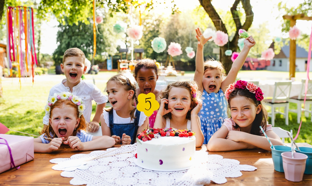 Children gathering outdoors with a birthday cake on the table