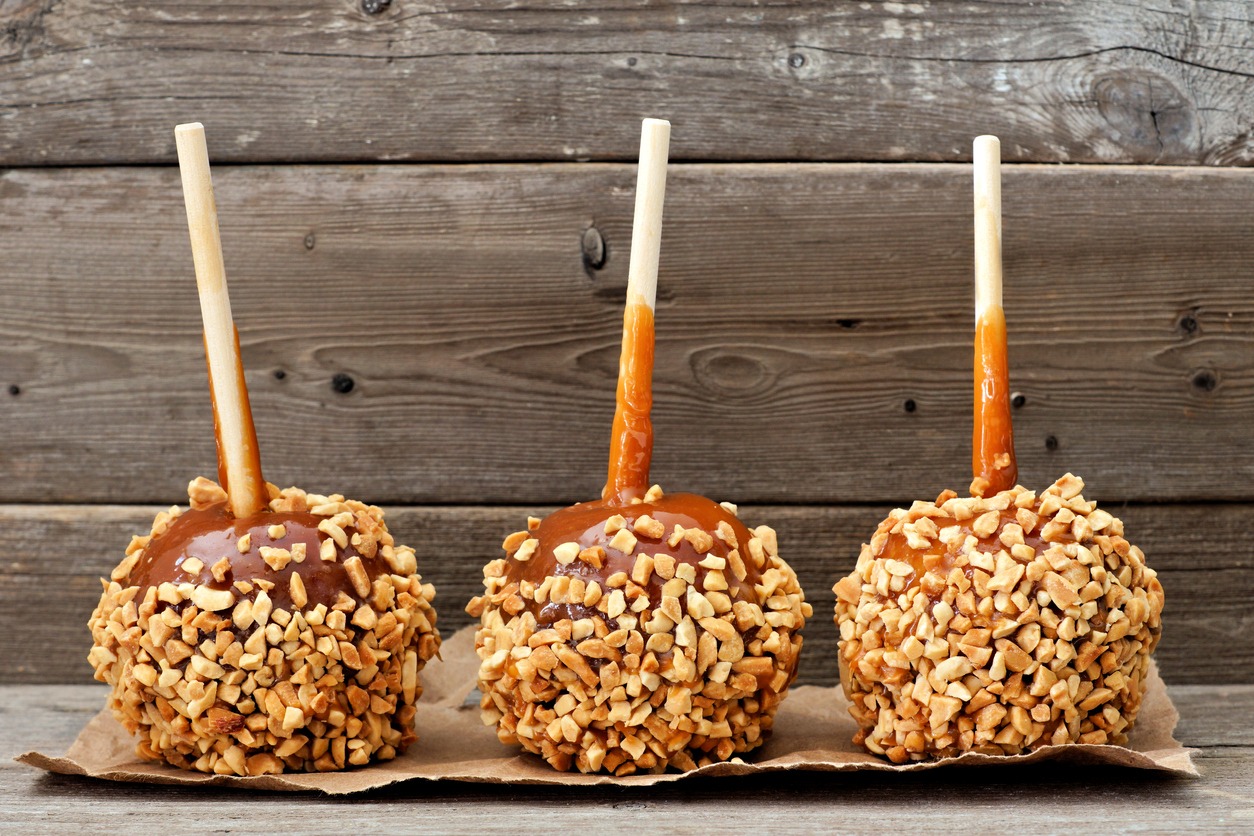 Three festive caramel apples with nuts against a rustic wood background