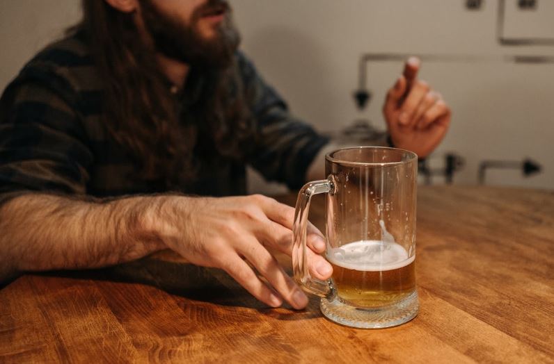 a man sitting in front of a table with his hand near an almost empty glass of beer