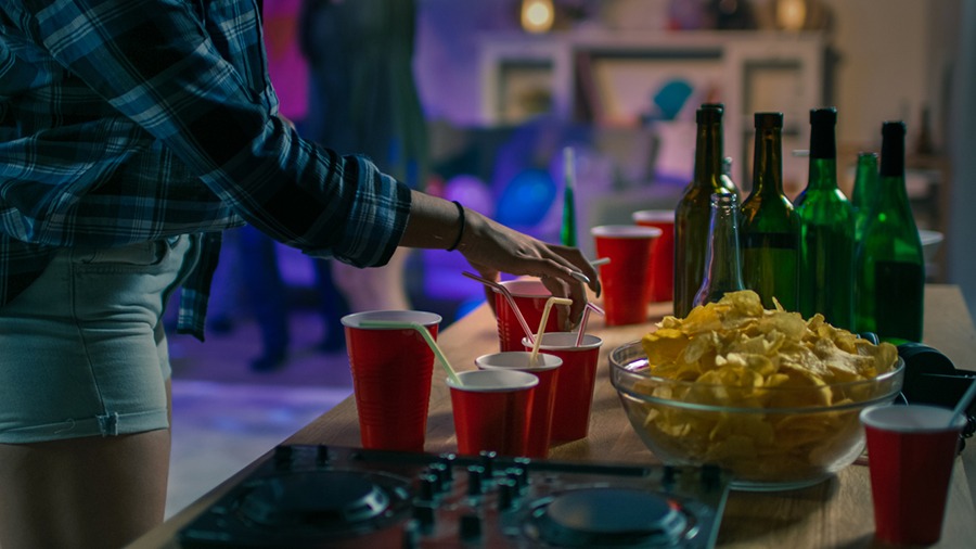 Girl takes a glass from the buffet table with chips and snacks at a house party