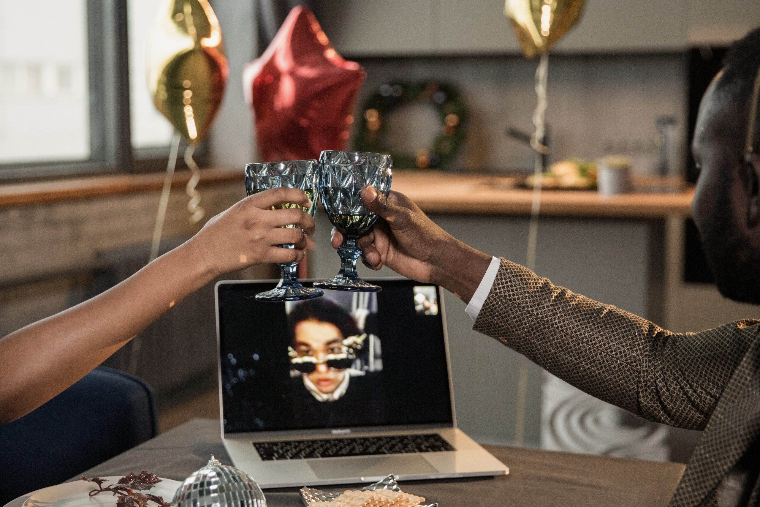 two people making a toast in front of a laptop while in a video conference with another woman