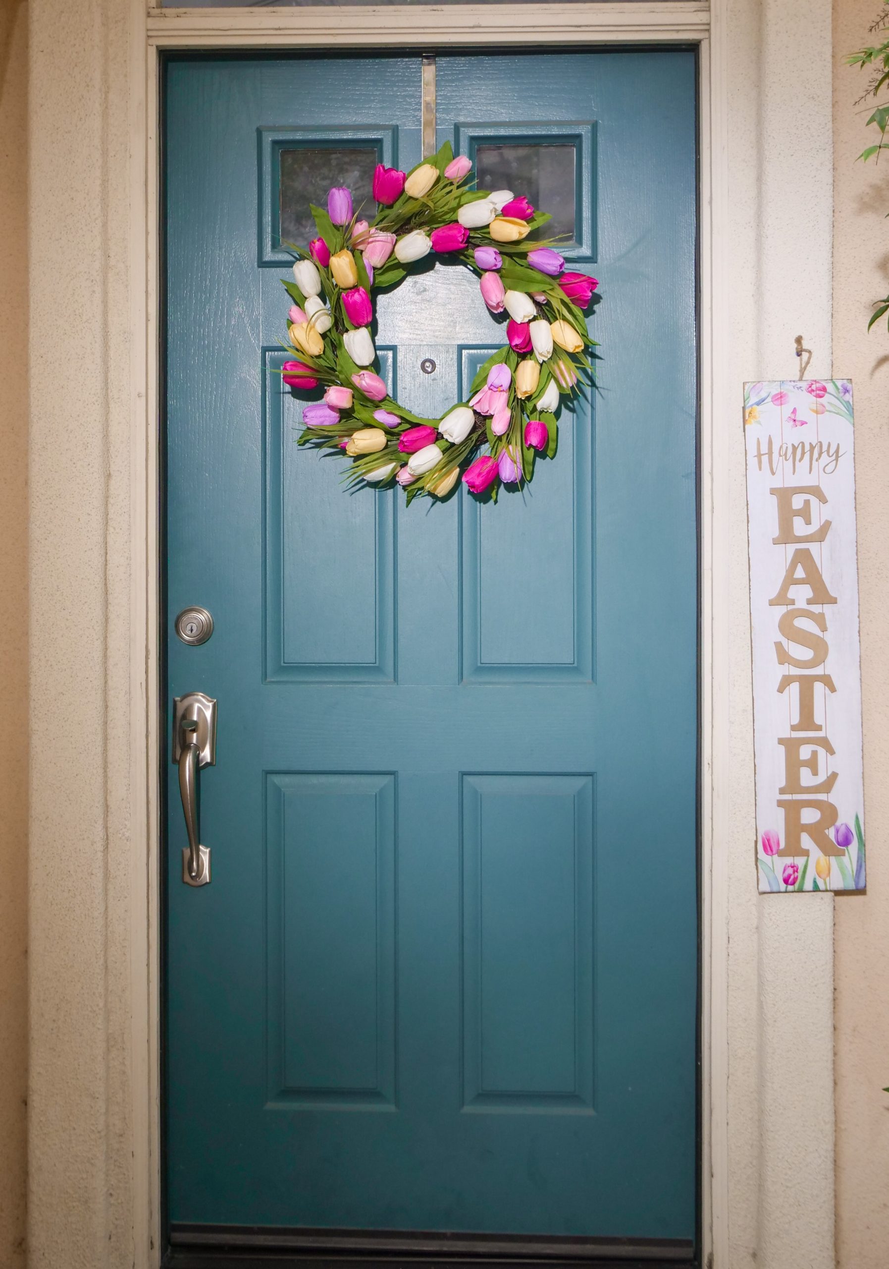 : Easter wreath made of tulips hanging on a wooden door with a Happy Easter sign on the side 