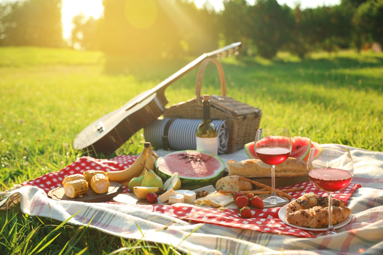 : a picnic blanket with delicious food and drinks outdoors on sunny day