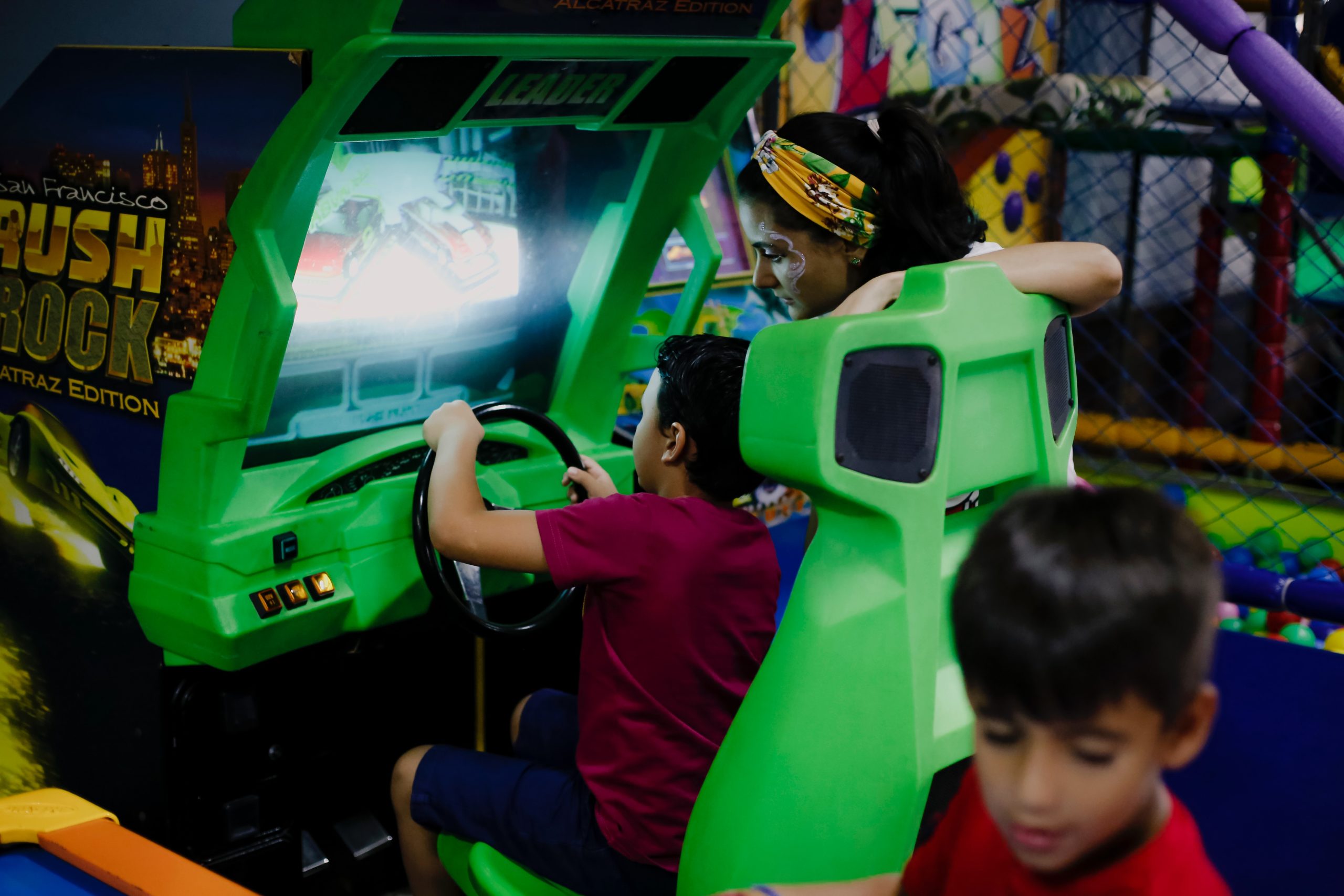 a boy playing a car racing simulator with his mother and sibling