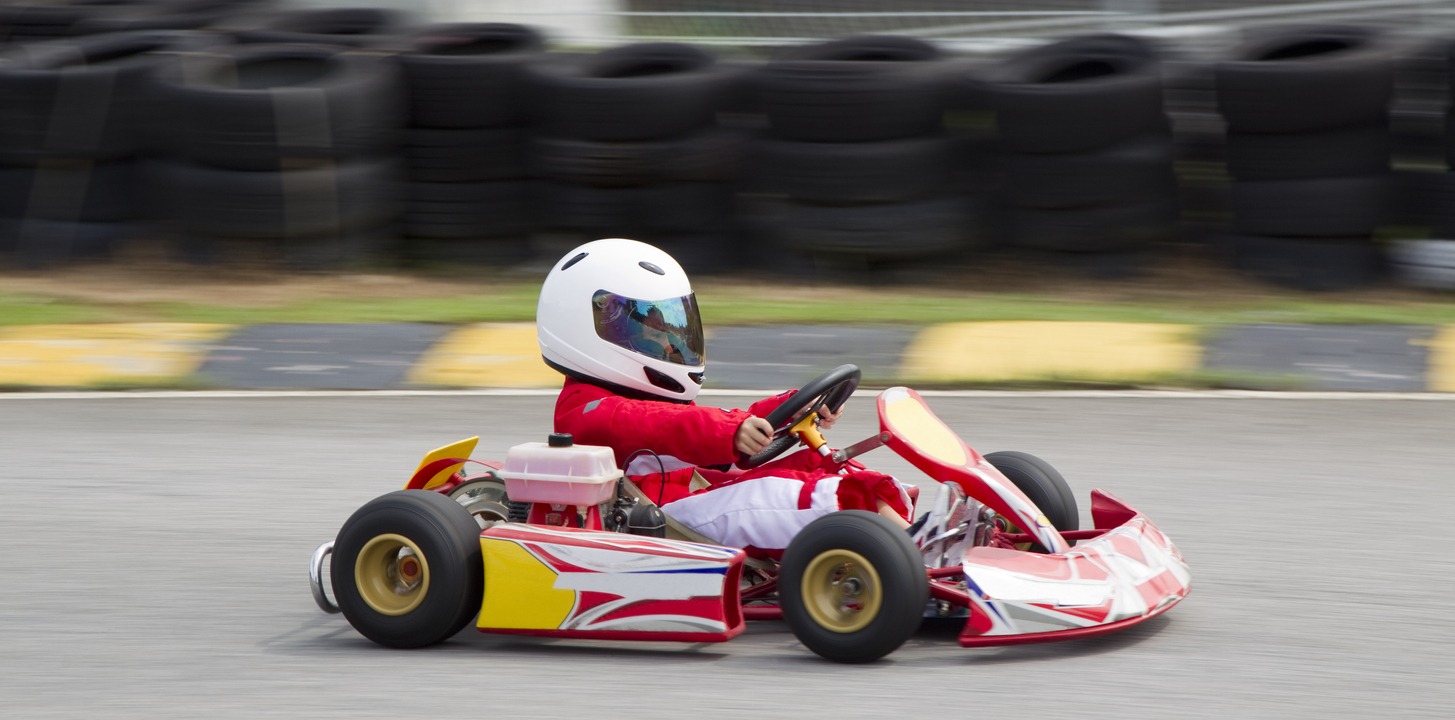 a boy wearing red and white race suit and white helmet driving a gokart