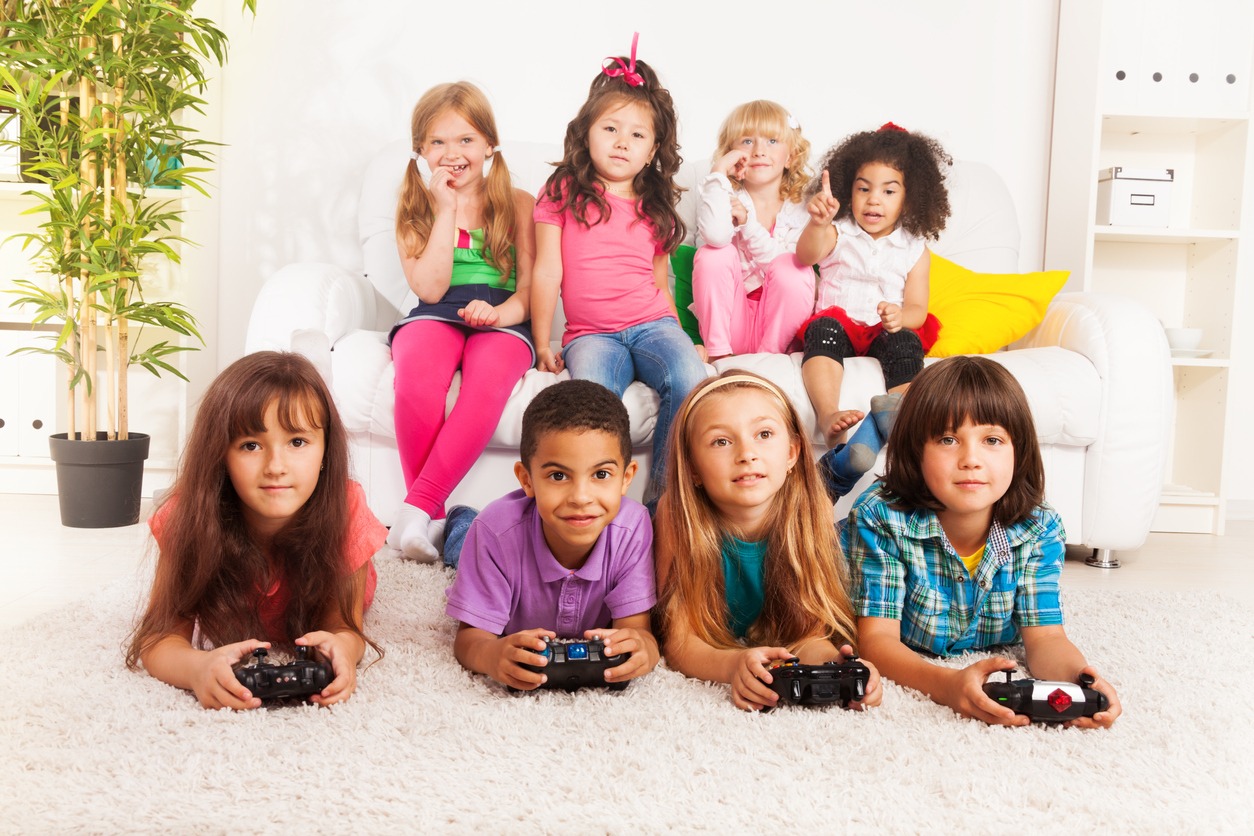 a group of kids playing videogames laying on the floor and sitting on the sofa in a room