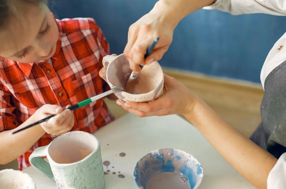 a crop artisan and little girl painting earthware in a workshop