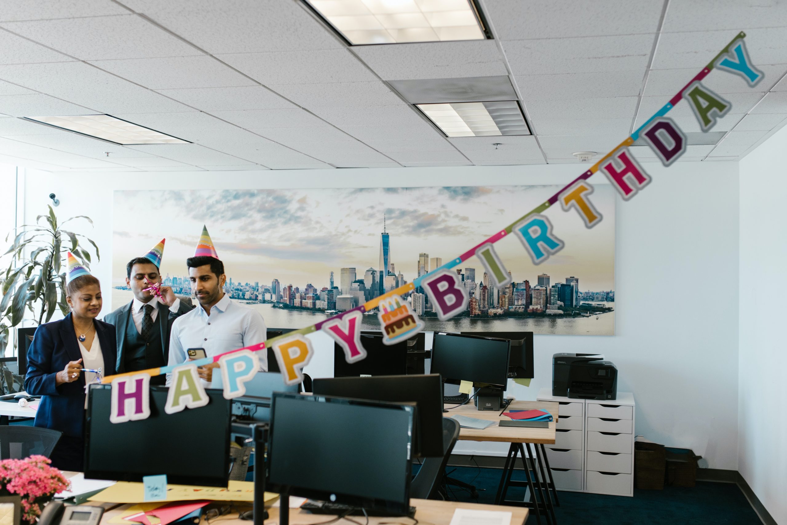  a happy birthday banner hanging inside the office with people wearing party hats