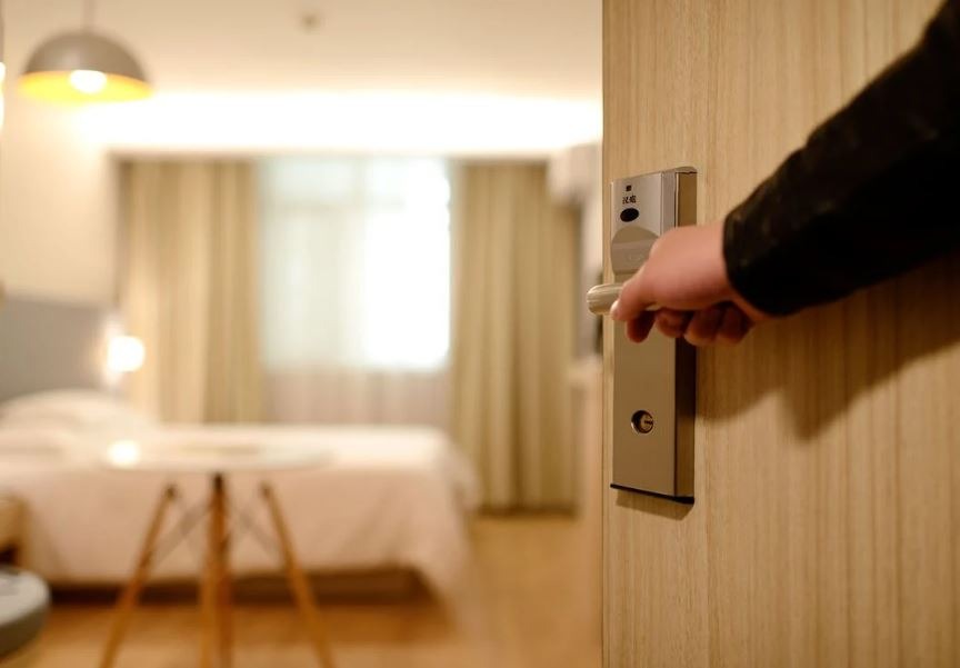 a person holding the hotel door open showing the bed inside