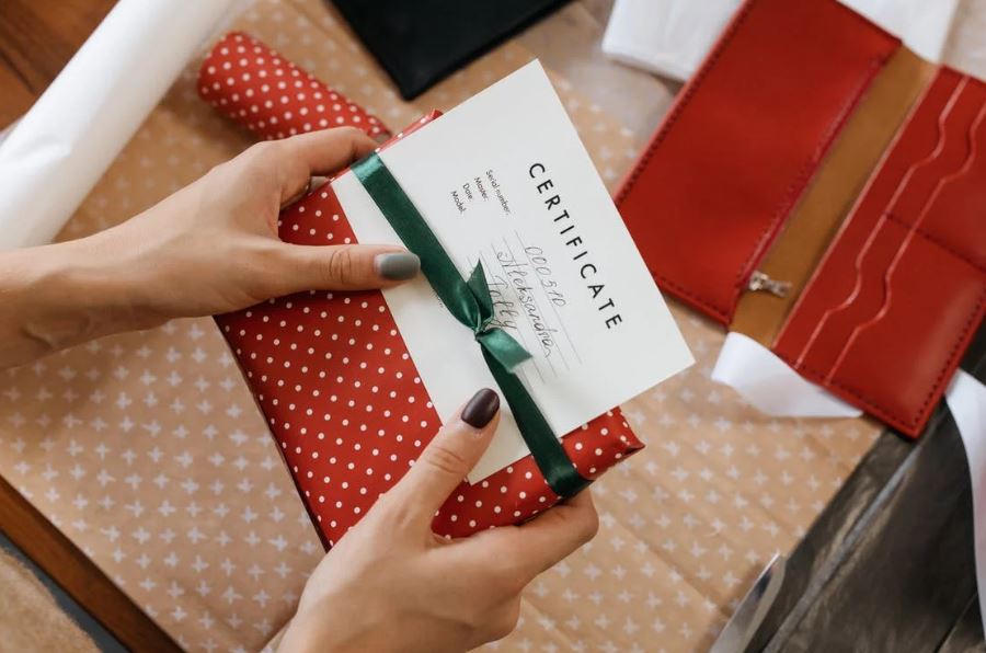 a person’s hands holding a gift certificate on top of a wrapped present