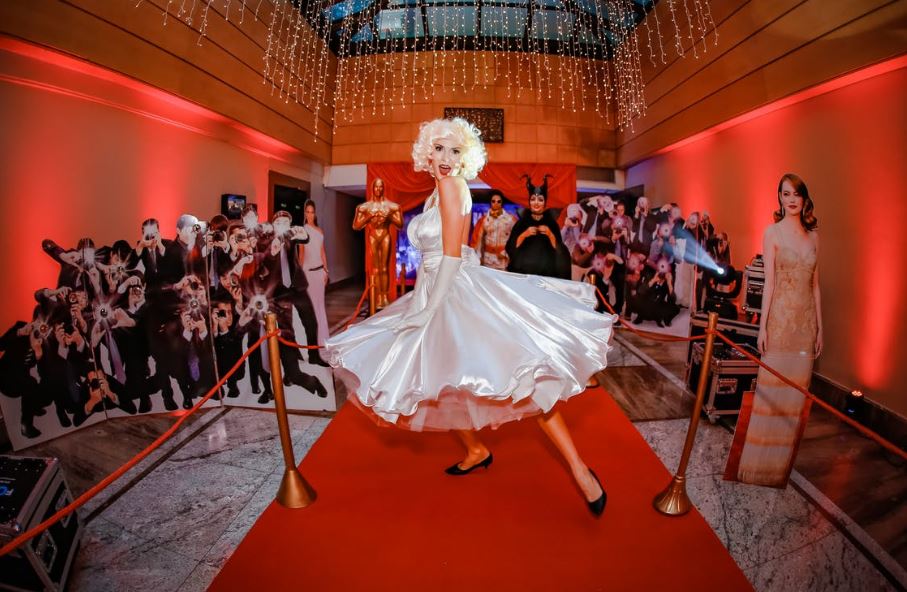 a woman dressed as Marilyn Monroe posing at a red carpet with standees of photographers and other stars