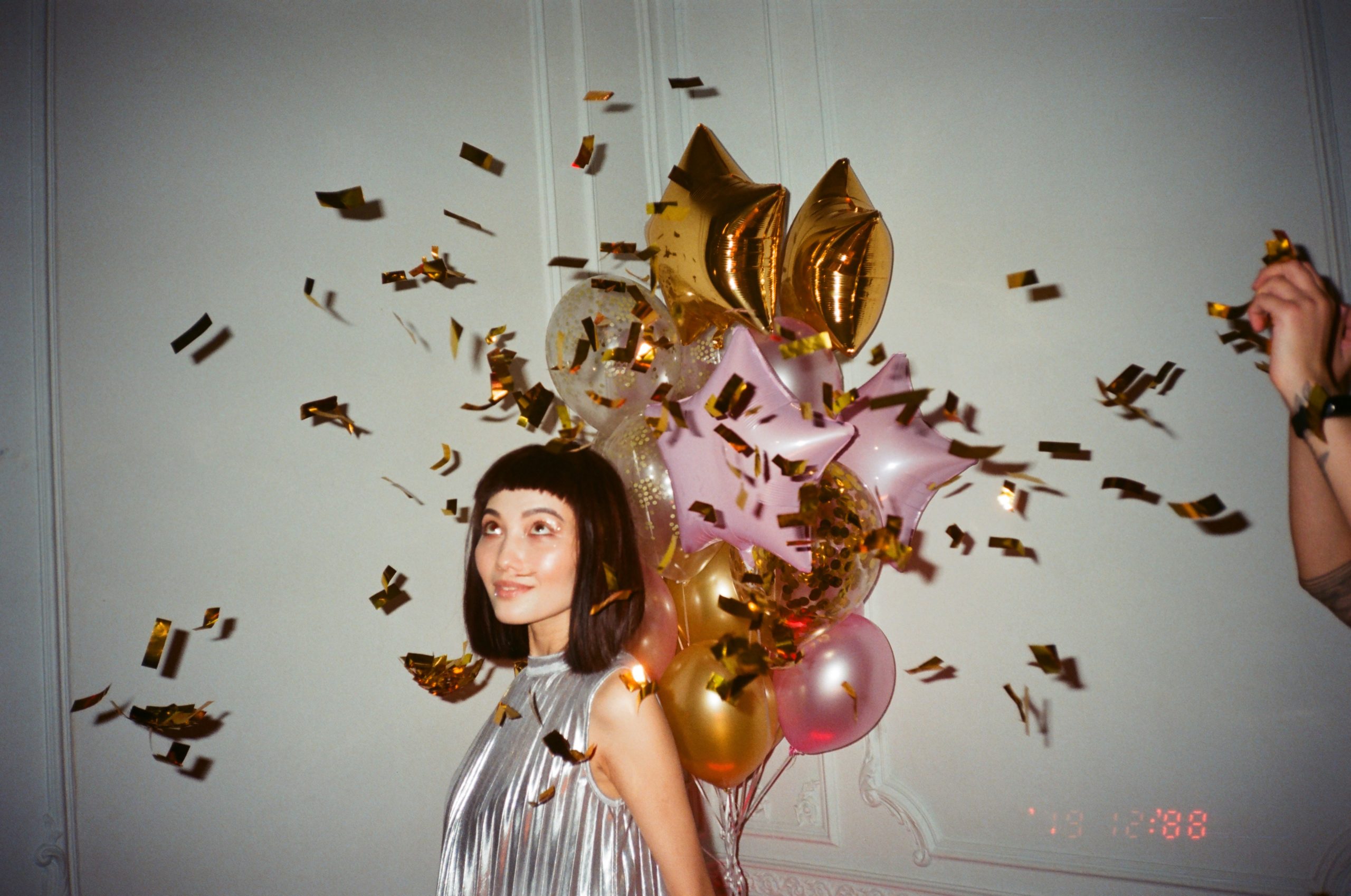 a woman posing in front of balloons and looking at the falling confettis