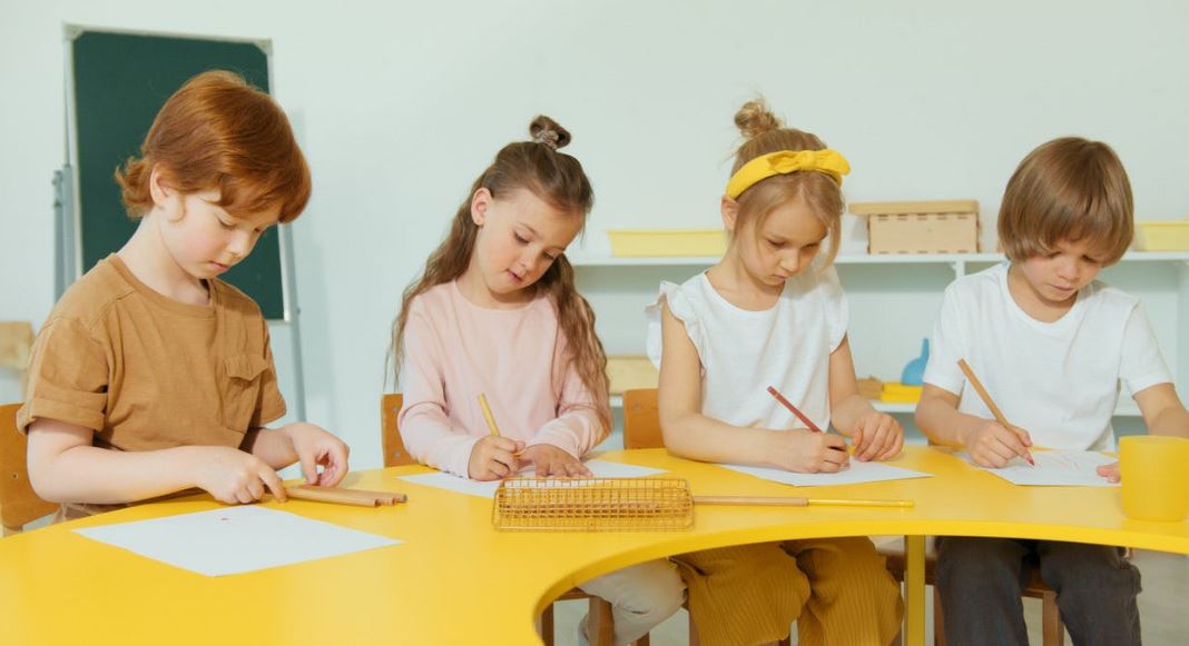 elementary students seated at a yellow table writing something on a paper