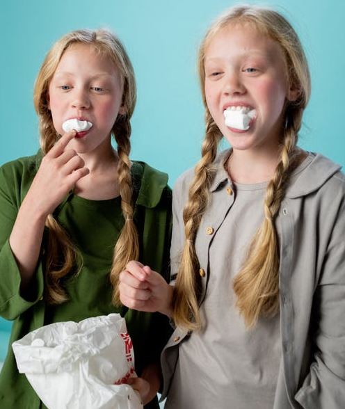 two girls with marshmallow in ther mouths