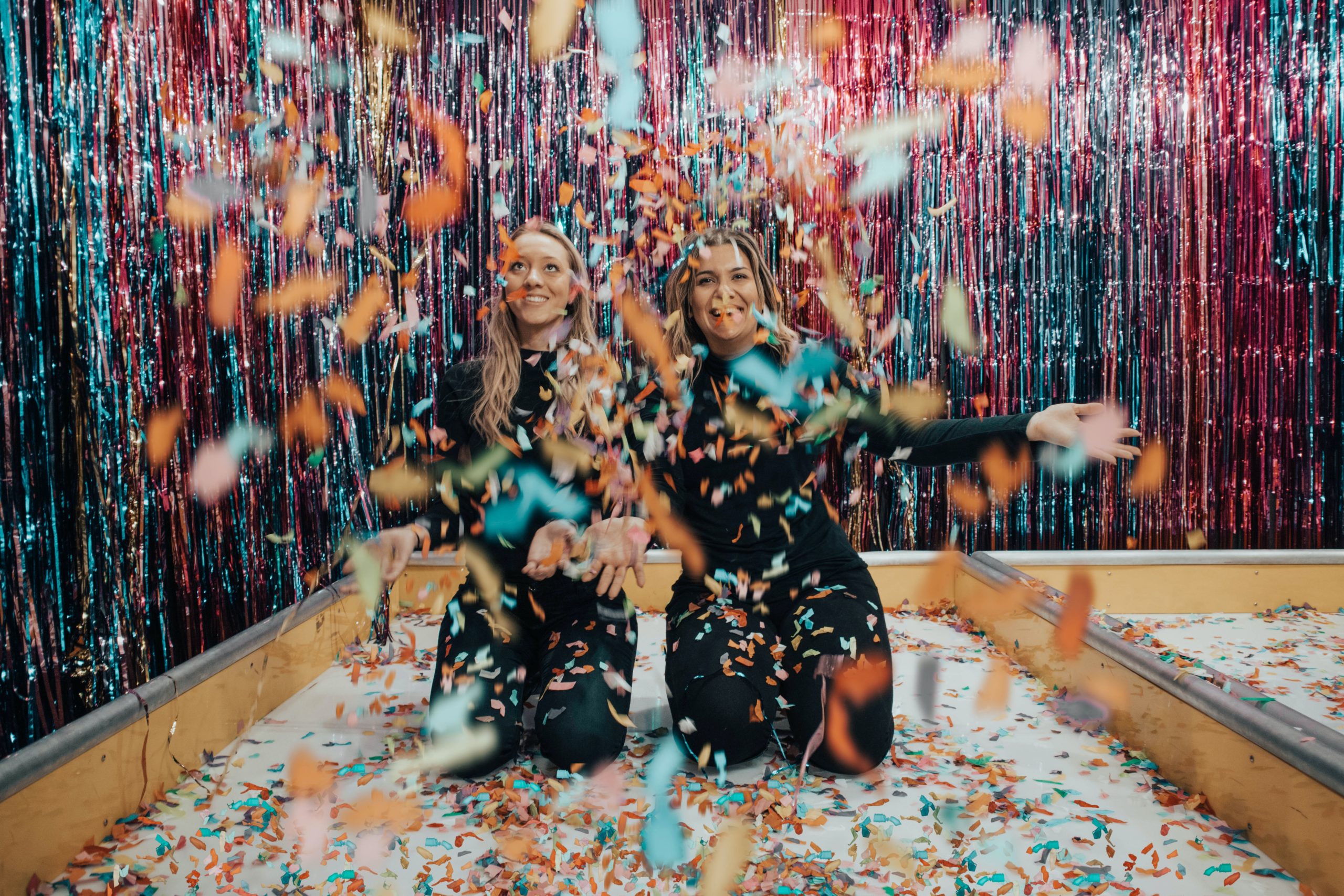 two women kneeling while throwing confetti