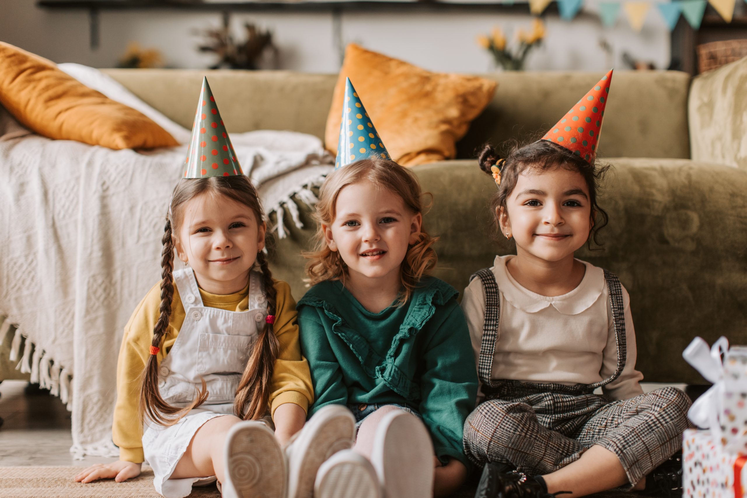 three little girls wearing party hats sitting on the floor