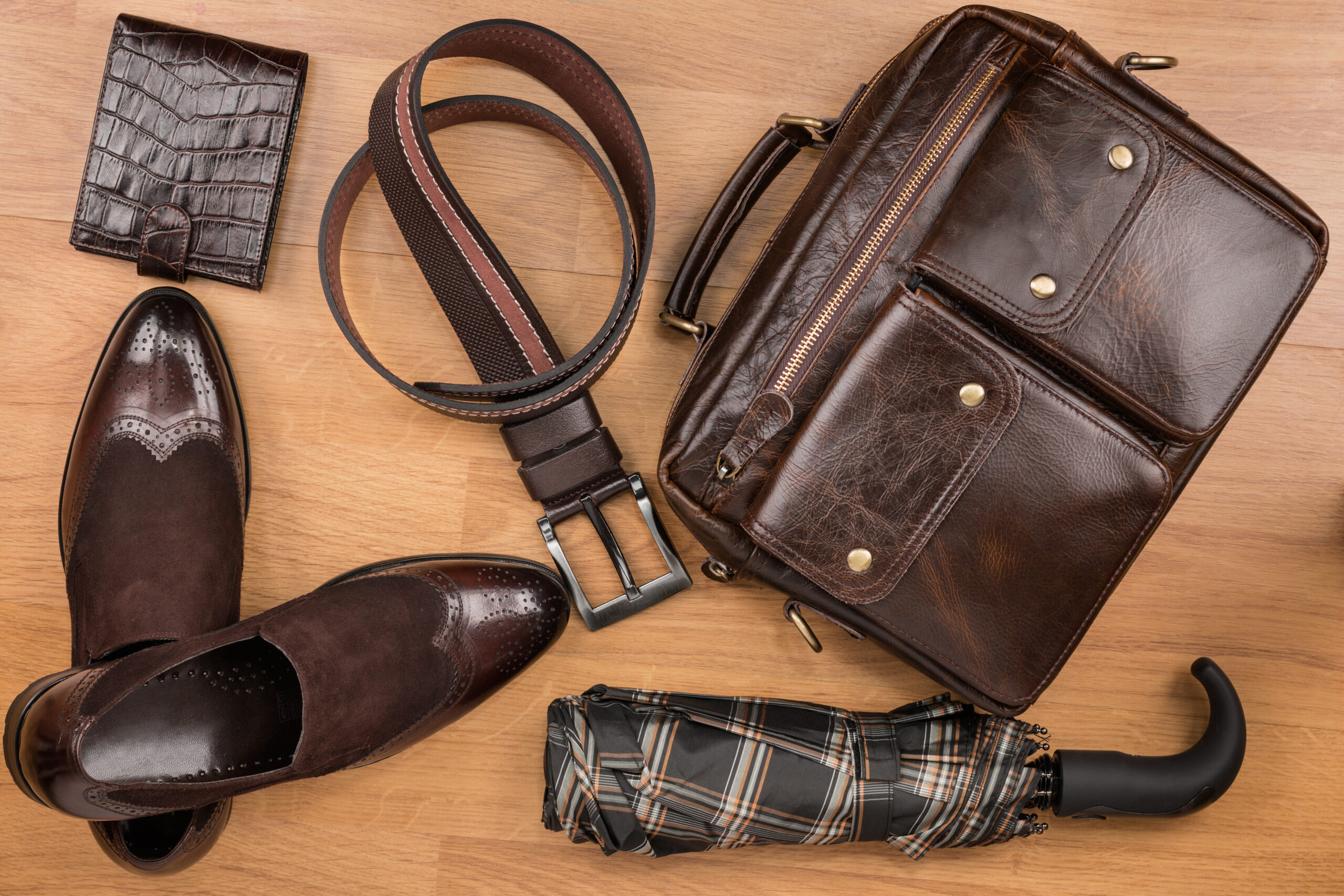 Classic brown shoes, briefcase, belt and umbrella on the wooden floor, can be used as background