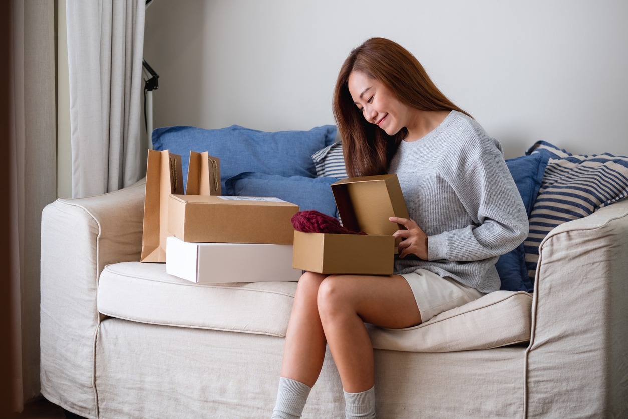 Young Asian woman feel excited unpacking gift box on couch in living room at home