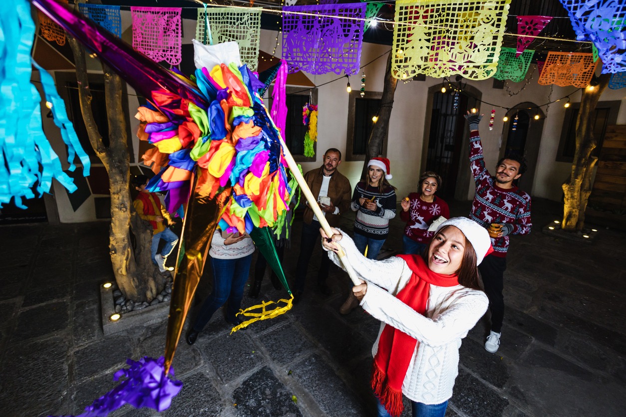 Hispanic young girl with Mexican family breaking a piñata at traditional posada party